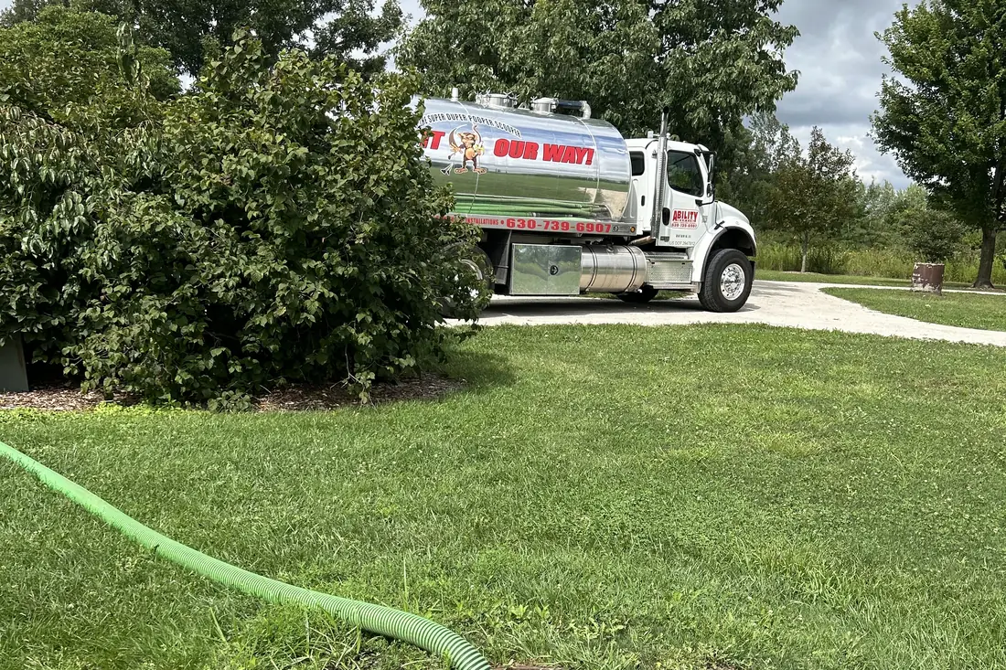 Ability truck pumping a residential septic tank on a tidy lawn
